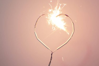 Kalp şekli kıvılcımlar saçıyor, pembe arka planda aşk kavramı var..