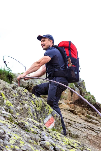 Young man hiking on difficult mountain trail with hanging cable — Stock Photo, Image