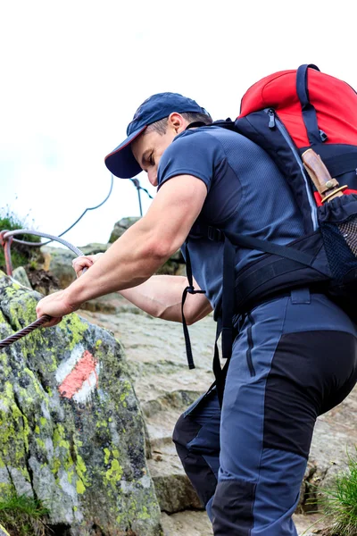 Young man hiking on difficult mountain trail with hanging cable — Stock Photo, Image