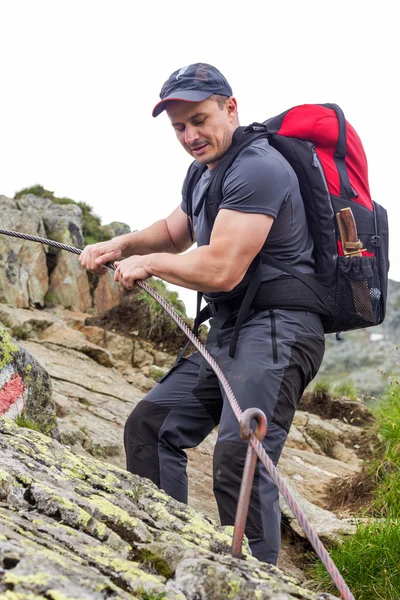 Young man hiking on difficult mountain trail with hanging cable — Stock Photo, Image