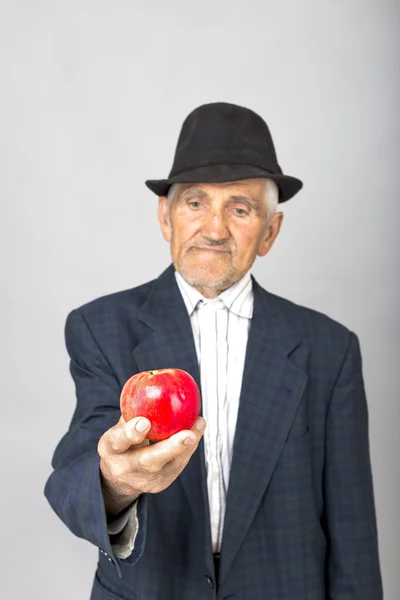 Portrait of a senior man with hat offering a red apple — Stock Photo, Image