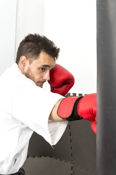 Young man in kimono throwing punches at a heavy punching — Stock Photo, Image