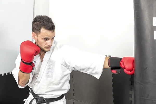 Joven en kimono lanzando puñetazos a un saco de boxeo pesado — Foto de Stock