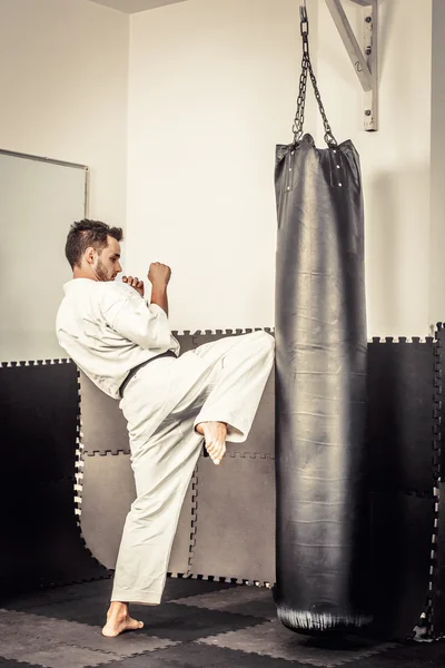 Athletischer schwarzer Gürtel Karate gibt einen kraftvollen Kniestoß während einer Stockbild