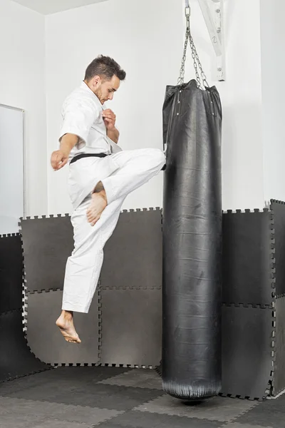Athletischer schwarzer Gürtel Karate gibt einen kraftvollen Kniestoß während einer Stockbild
