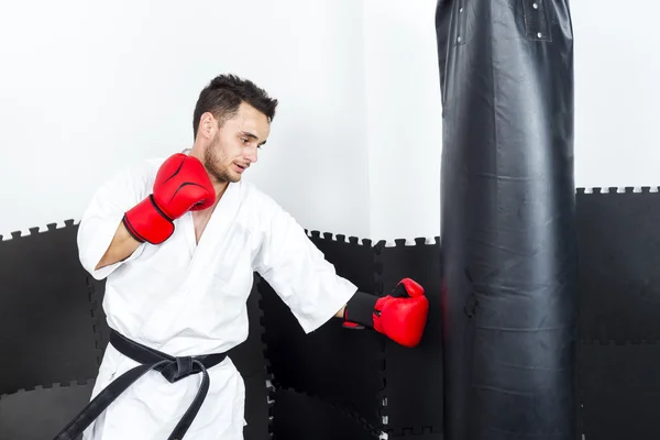 Joven en kimono lanzando puñetazos a un saco de boxeo pesado — Foto de Stock