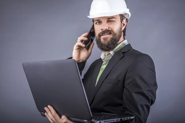 Ingeniero exitoso hablando por teléfono y sosteniendo su computadora portátil —  Fotos de Stock