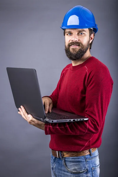 Junger Ingenieur mit Hut steht während er an seinem Laptop arbeitet — Stockfoto