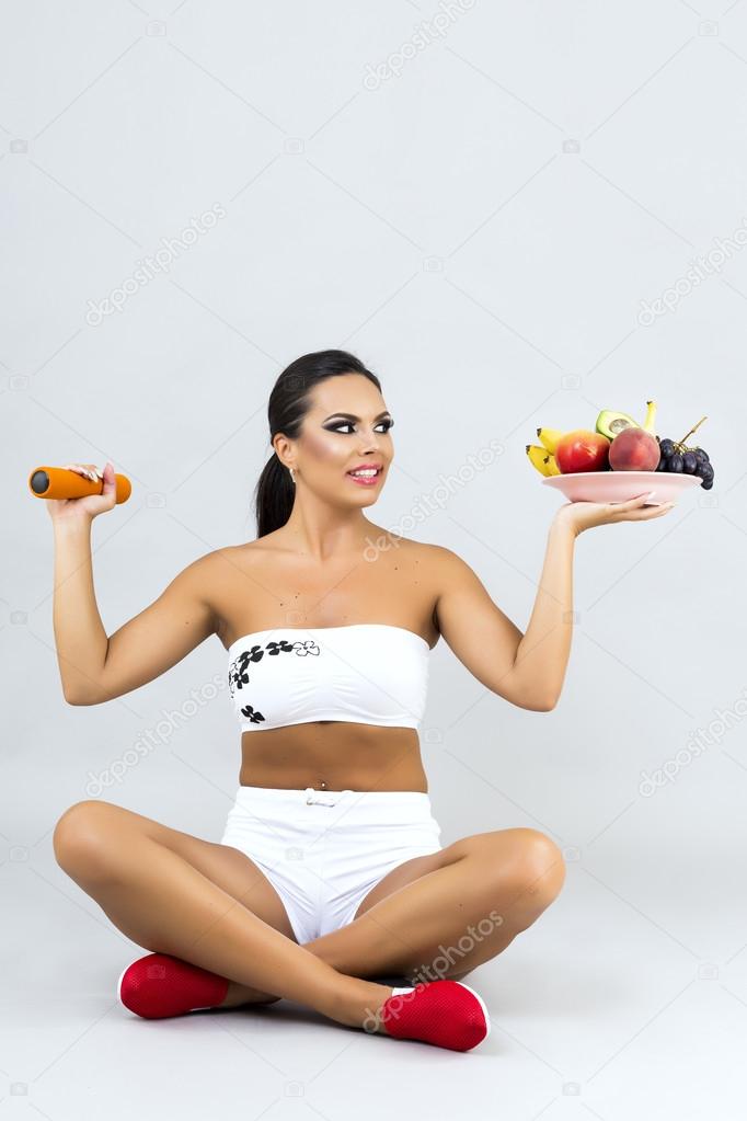 Happy young woman holding a plate with fruits in one hand and du