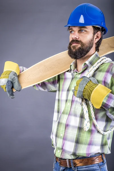 Porträtt av en ung snickare med hård hatt hålla trä planka — Stockfoto