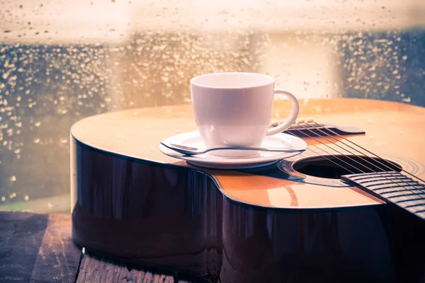 Coffee cup and acoustic guitar next the window with drop water