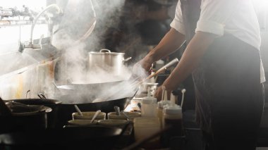 Şef mutfakta yemek pişirmekle meşgul. Şef kızartma tavasında yemek pişirir, sigara içer ve sosu mutfağa döker..
