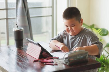 Şirin Asyalı çocuk evde tabletten ders öğreniyor. Sosyal uzaklık kavramı.