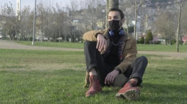 Maskeli genç adam parkta oturuyor.