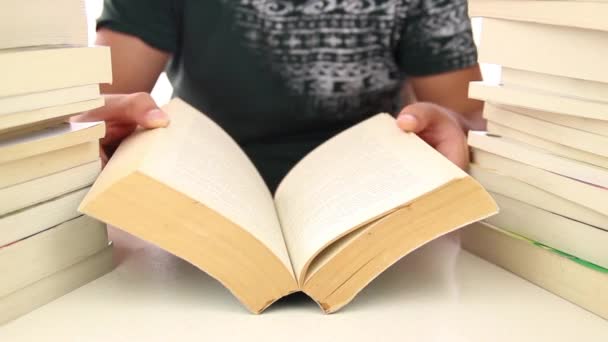 Erkek öğrenci kitap yığınları arasında oturmuş kitap okuyor. — Stok video