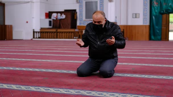 Старик в маске поднимает руки и молится из мечети — стоковое видео
