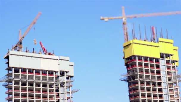 Un edificio de la ciudad está siendo hecho por dos enormes grúas blancas de construcción — Vídeos de Stock