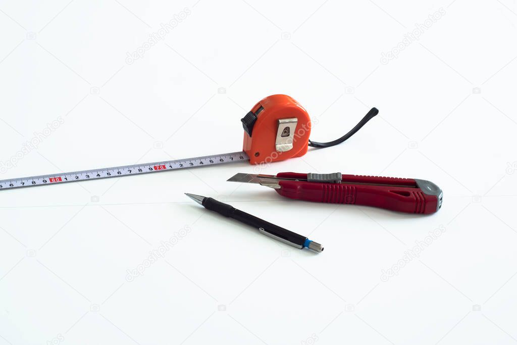 Working tools: tape measure, knife and pencil on white plastic.