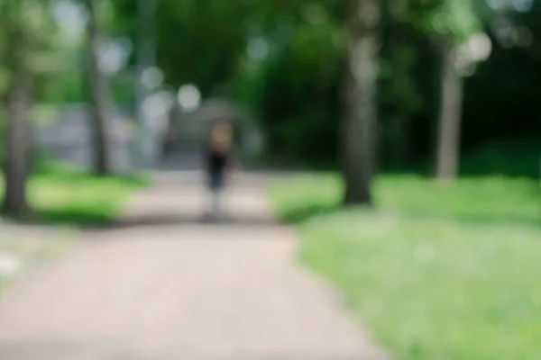 The park. Green summer trees. Human\'s figure. Blurred image with bokeh effect.