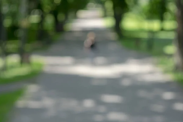 The park. Green summer trees. Human\'s figure. Blurred image with bokeh effect.