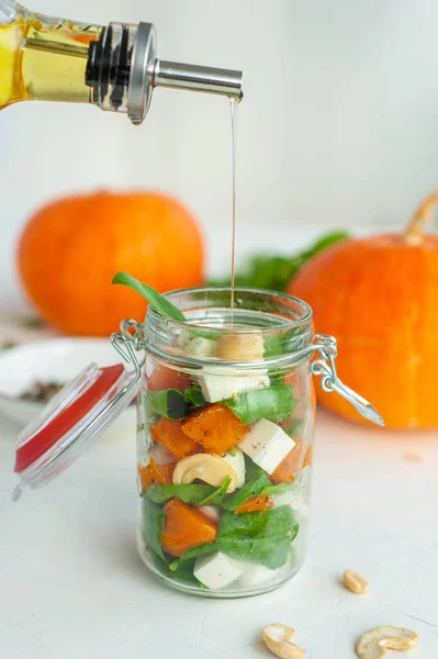 Ensalada de calabaza, espinacas y feta en un frasco. Un aperitivo ligero. Sobre un fondo brillante. — Foto de Stock