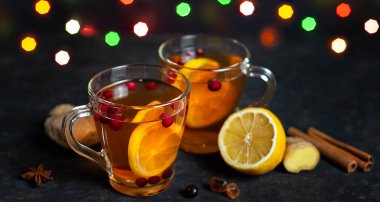 Noel vitamini çayı. İçinde kızılcık, limon ve zencefil olan cam bardakta çay ve Noel ışıkları. Pankart.