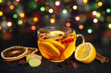 Limon, kızılcık ve zencefilli sıcak kokulu bir kış içeceği karanlık bir masada, büyük bir cam bardakta Noel ışıklarının önünde. Noel meyveli çayı.