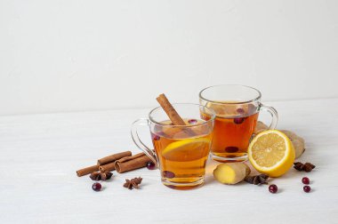 Kışın ısınan çay. Beyaz ahşap arka planda iki bardak çay, limon, zencefil ve kızılcık. Boşluğu kopyala.