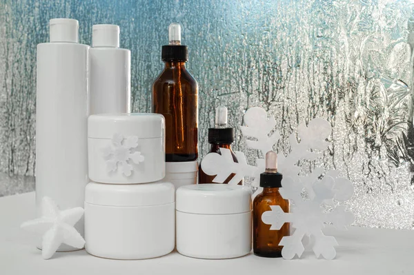 A set of winter care cosmetics against the background of the frosty window. White jars, bottles and vials on a white background. — Stock Image A set of winter care cosmetics against the background of the frosty window. White jars, bottles and vials on a white background. Royalty Free Stock Images