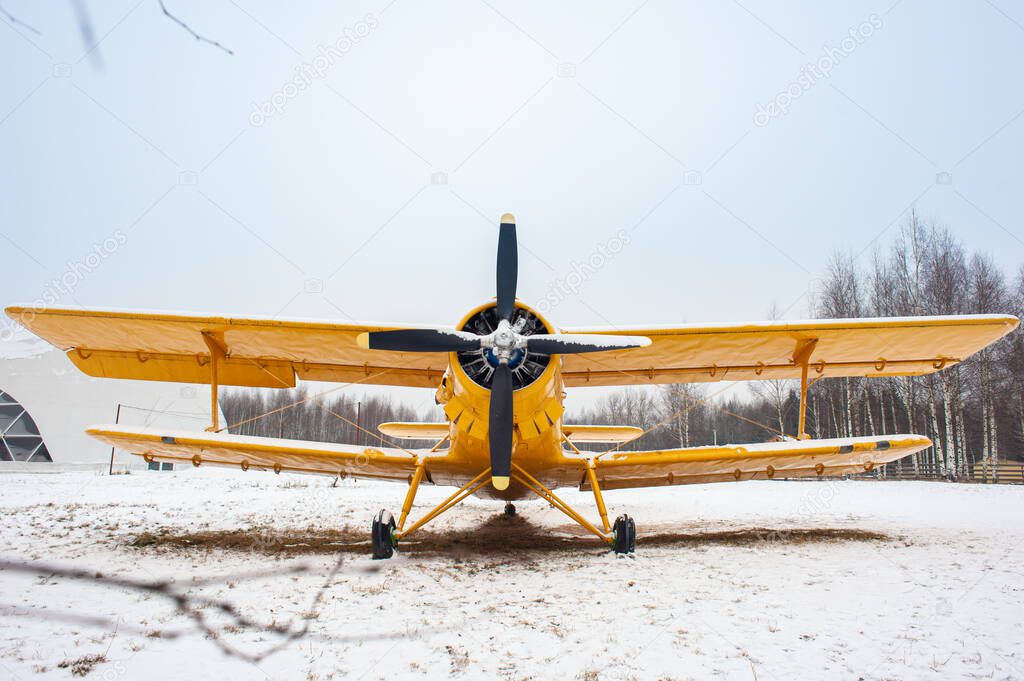 A small yellow plane with a propeller in front and two pairs of wings on a snow-covered field.