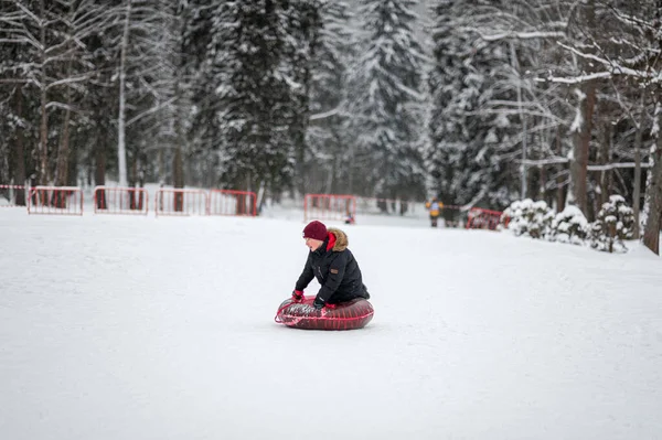 Active winter leisure. Tubing. A teenage boy rolls down a hillside in the woods on a tube. — Stock Photo, Image