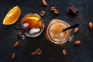 Buzlu soğuk espresso kahve ve iki bardak portakal suyu fındık, çikolata ve portakallı karanlık bir masada. Canlandırıcı bir yaz içkisi. Yukarıdan görüntüle.