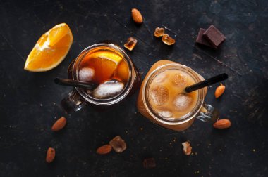 Buzlu soğuk espresso kahve ve iki bardak portakal suyu fındık, çikolata ve portakallı karanlık bir masada. Hareketli bir yaz içkisi. Yukarıdan görüntüle.