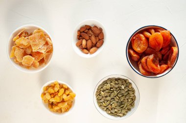 Arka planda beyaz tabaklarda farklı kurutulmuş meyve ve fındıklar var. Sağlıklı bir atıştırmalık Kış vitaminleri. Yukarıdan görüntüle. 