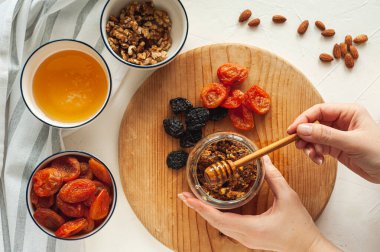 Kurutulmuş meyve, fındık ve baldan oluşan sağlıklı bir vejetaryen tatlı yapma süreci. Malzemeler beyaz bir masada. Yukarıdan bak. Evde yemek tecrübeleri.