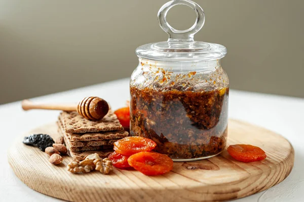 Healthy vitamin vegan dessert. A mixture of dried fruits, nuts, honey and lemon in a jar on a wooden board. Selective focus.