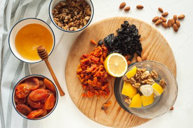 Kurutulmuş meyve, fındık ve baldan oluşan sağlıklı bir vejetaryen tatlı yapma süreci. Malzemeler beyaz bir masada. Yukarıdan bak. Evde yemek tecrübeleri.