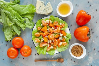 Hurma, mandalina ve küflü peynirli hafif tatlı ve ekşi salata. Mavi bir masada kışın vitamin salatası ve malzemeler. Diyet yemek. Yukarıdan görüntüle. 