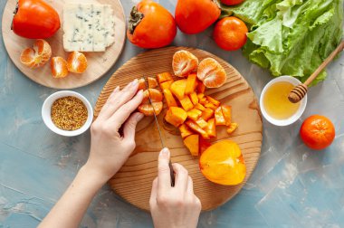 İçindekiler ve hurma, mandalina ve mavi peynirli vitamin kış salatası yapma süreci. Adım adım. Kadın mandalinayı yuvarlak bir tahta üzerinde kesiyor. Yukarıdan görüntüle.
