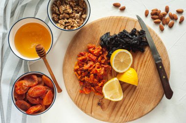 Kurutulmuş meyve, fındık ve baldan oluşan sağlıklı bir vejetaryen tatlı yapma süreci. Malzemeler beyaz bir masada. Yukarıdan bak. Evde yemek tecrübeleri.