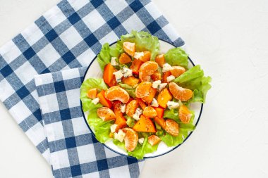 Mandalina ve mavi peynirli açık parlak hurma salatası mavi peçeteli beyaz bir masada. Kış vitamini diyeti. Yukarıdan görüntüle.