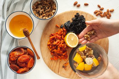 Kurutulmuş meyve, fındık ve baldan oluşan sağlıklı bir vejetaryen tatlı yapma süreci. Malzemeler beyaz bir masada. Yukarıdan bak. Evde yemek tecrübeleri.