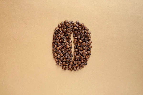 Жареные кофейные зерна выложены в виде большого зерна кофе на бежевом фоне. Монохром. — стоковое фото