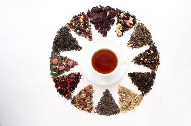 Böğürtlenli farklı çay ve bitkisel karışımlar beyaz arka planda beyaz bir fincan çay etrafında bir daire şeklinde dizilmiştir. Çay içme zamanı. Yukarıdan bak. Sağlıklı içecekler.