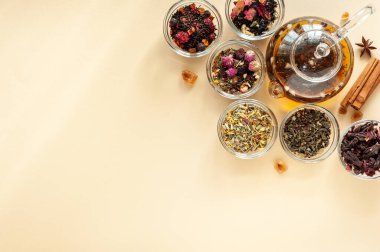 Çaydanlığın yanındaki yeşil, siyah ve bitkisel çayın farklı türleri bej arka planda sıcak demlenmiş çayla dolu. Lezzetli organik içecekler. Yukarıdan bak. Metin için bir yer.