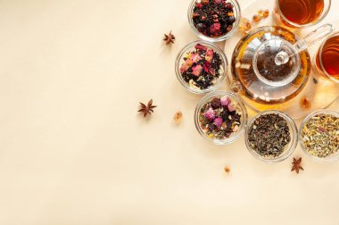 Çaydanlığın yanındaki yeşil, siyah ve bitkisel çayın farklı türleri bej arka planda sıcak demlenmiş çayla dolu. Lezzetli organik içecekler. Yukarıdan bak. Metin için bir yer.