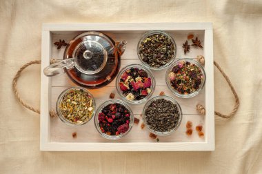 çeşitli bitkisel ve dut çayı çeşitleri ve ahşap tepside taze çay ve bej keten masa örtüsü ile bir çaydanlık. Yukarıdan görüntüle.