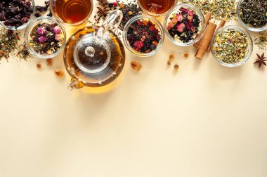 Çaydanlığın yanındaki yeşil, siyah ve bitkisel çayın farklı türleri bej arka planda sıcak demlenmiş çayla dolu. Lezzetli organik içecekler. Yukarıdan bak. Metin için bir yer.