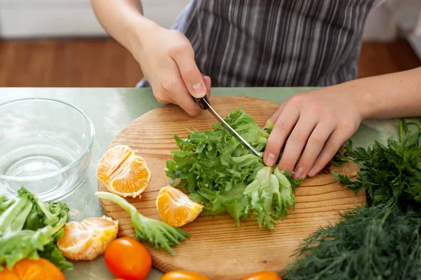 Un adolescent prépare une salade de fruits sur une recette d'Internet. Le garçon coupe de la laitue sur la table de la cuisine, devant lui se trouve un ordinateur portable. L'enfant est engagé dans des tâches ménagères. — Photo