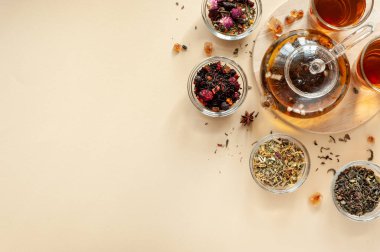 Çaydanlığın yanındaki yeşil, siyah ve bitkisel çayın farklı türleri bej arka planda sıcak demlenmiş çayla dolu. Lezzetli organik içecekler. Yukarıdan bak. Metin için bir yer.